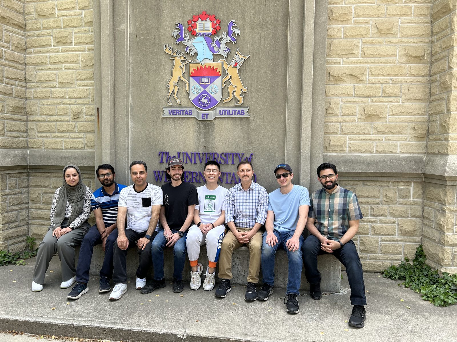 Lab members sitting together below the Western crest on a stone wall on campus