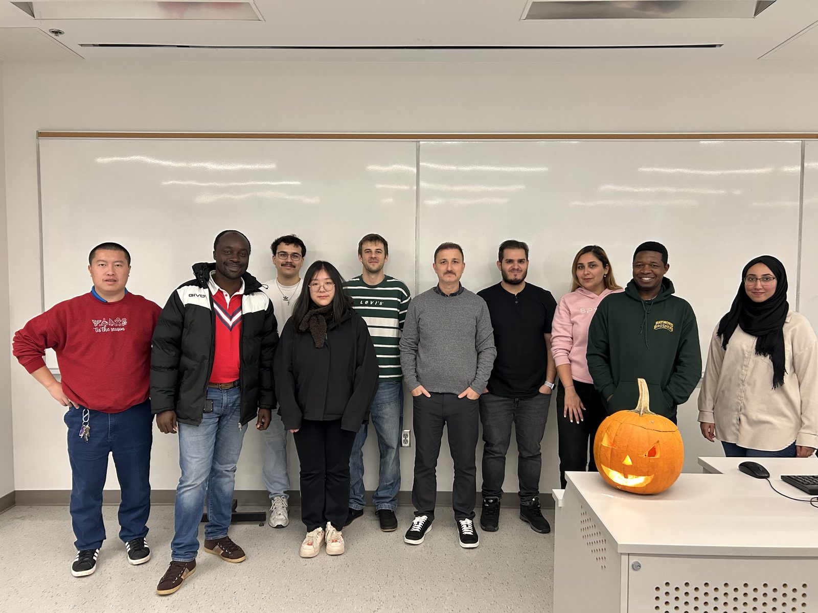 Lab members standing in a seminar room beside a carved pumpkin
